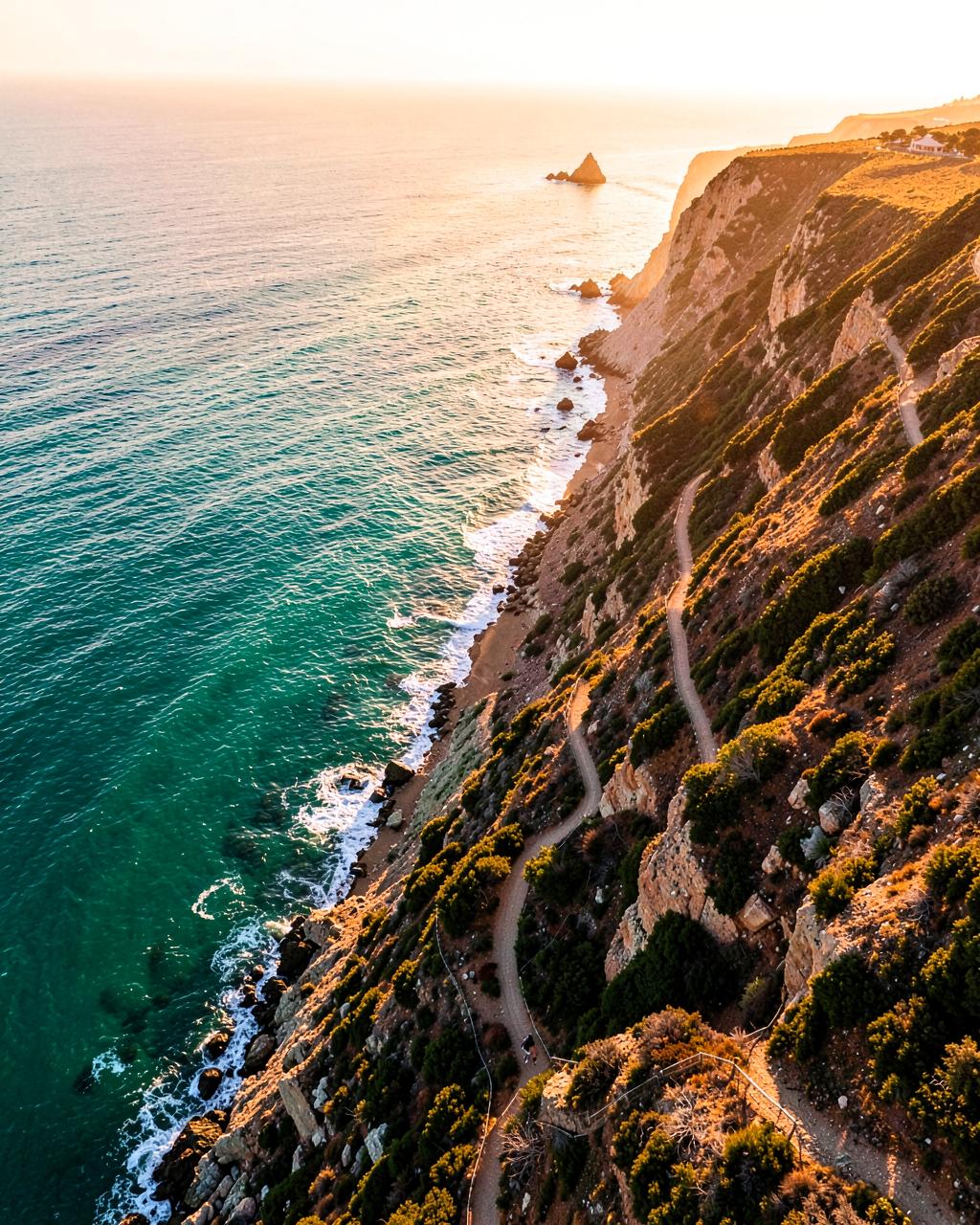 Coastal cliff path meeting turquoise sea at golden hour